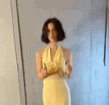 a woman in a yellow dress is standing in front of a wall .