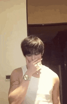 a man wearing a white tank top is covering his mouth with his hand .