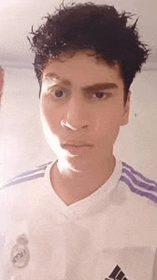 a young man with curly hair is making a funny face while wearing a white shirt with purple stripes .