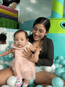a woman is holding a baby in her arms in a ball pit
