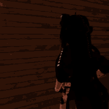 a woman with long black hair is standing in front of a wooden wall and pointing at something .