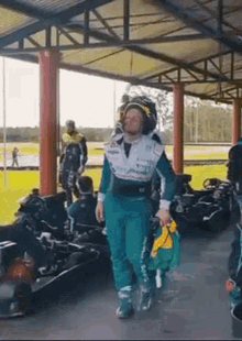 a man in a racing suit is walking in front of a row of go karts on a track .