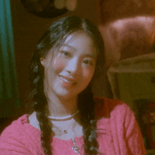a woman wearing a pink sweater and a pearl necklace smiles
