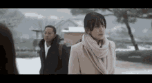 a man and a woman are standing in the snow . the woman is wearing a scarf around her neck .