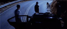 a group of people standing on the side of a road with a car in the foreground