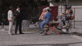 a group of people standing around a picnic table with one wearing a cowboy hat