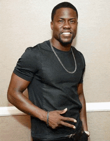 a man wearing a black t-shirt and a chain is standing in front of a wall .