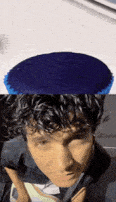 a man with curly hair is wearing a blue hat and a blue cupcake on his head .
