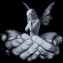 a black and white photo of a woman with wings sitting on a man 's hands .