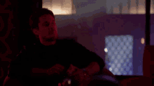 a man is smoking a cigarette in a dark room while sitting at a table .