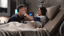 a man and a woman are laying in a hospital bed and the man is touching the woman 's face