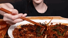 a woman is eating noodles with chopsticks from a plate .