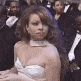 a woman in a white dress is sitting in a crowd of people and looking at the camera .