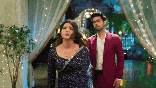 a man in a pink suit and a woman in a blue dress are walking down a staircase .