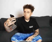 a man wearing a black shirt that says amiri is sitting on a couch