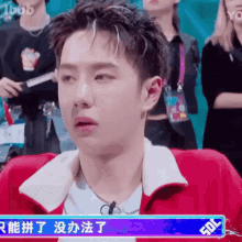 a young man in a red jacket is sitting in front of a crowd of people .