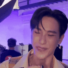 a young man is smiling with his eyes closed in a room with purple lights .