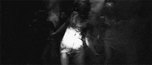 a black and white photo of a group of zombies walking through a dark room .