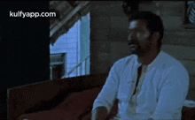 a man with a beard is sitting on a couch in a dark room .