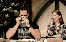 a man wearing a shirt that says mighty gin is drinking from a mug next to a woman
