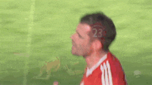 a man in a red adidas jersey is standing on a soccer field with his mouth open .