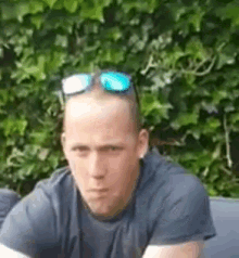 a man wearing sunglasses and a gray shirt is sitting on a couch .