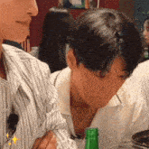 a man in a striped shirt is sitting at a table with a green bottle of beer .