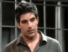 a man in a green shirt is standing in front of a window and making a funny face .