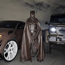 a man in a batman costume is standing in front of a car and a jeep .
