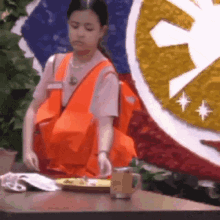 a girl in an orange vest is standing in front of a table