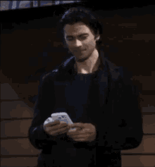 a man in a black jacket is standing in front of a wooden wall and holding a pen .