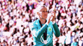 a woman wearing a green shirt with the letter w on it is clapping in front of a crowd