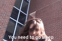 a woman standing in front of a brick building with the words " you need to go sleep " written on the bottom