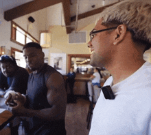 a man wearing glasses is standing in a restaurant talking to another man