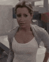 a woman in a white tank top is standing in a bathroom with her hands on her hips .