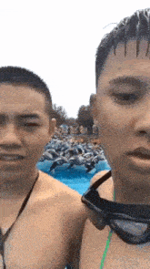 two shirtless men wearing goggles are standing next to each other in front of a crowd of people in a pool .