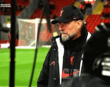 a man with a beard wearing a black nike hat and a black jacket with the letter a on it