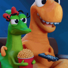 two dinosaurs are sitting on a couch eating popcorn and holding a remote