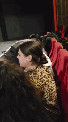 a woman in a leopard print shirt sits in a theater watching a movie
