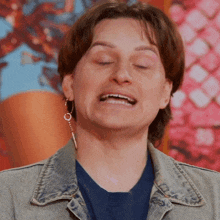 a woman wearing a blue shirt and a denim jacket is making a funny face with her eyes closed