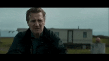 a man in a black jacket stands in front of a trailer .