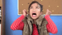 a young girl wearing a fur vest is making a funny face .