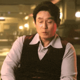 a man with his eyes closed is wearing a brown vest and white shirt