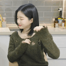 a woman in a green sweater is sitting in a kitchen with her eyes closed