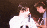 a man singing into a microphone while another man looks on