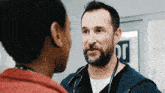 a man with a beard and a stethoscope is talking to another man .