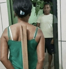 a woman in a green tank top is standing in front of a mirror with a wooden stick in her back .