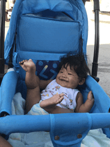 a baby is laying in a blue stroller and smiling at the camera