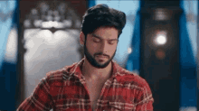 a man with a beard is wearing a red plaid shirt and looking down .