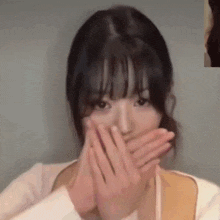 a woman is covering her mouth with her hands and looking at the camera .